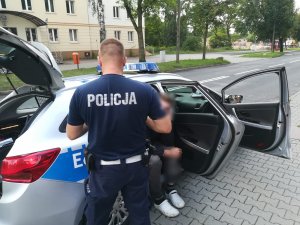 Policjant stojąc przy radiowozie sprawdza kierującego motorower.