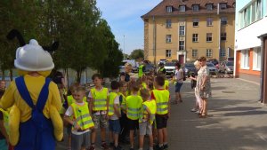 Zdjęcie przedstawia człowieka maskotke, dzieci i nauczycielki stojące na placu szkoły