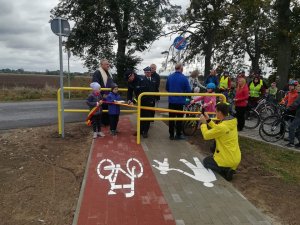 Na zdjęciu widoczny jest opiekun robiący zdjęcie dzieciom w raz z policjantem na ścieżce rowerowej.