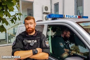 Zdjecie przedstawia policjanta, który uczestniczył w ratowaniu życia mężczyzny, stojącego obok policyjnego busa.