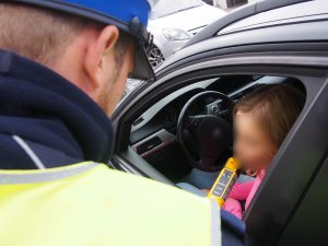 Zdjęcie przedstawia policjanta, który sprawdza trzeźwość kierującej alkomatem.