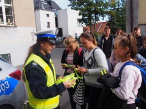 Zdjęcie przedstawia policjantkę, która rozdaje odblaski dzieciom.