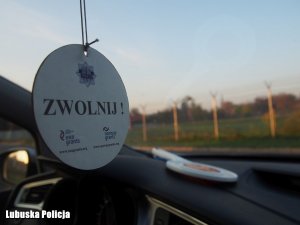 Zdjęcie przedstawia zawieszkę do samochodu, na której widnieje napis: zwolnij.