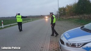 Zdjęcie przedstawia dwóch policjantów zatrzymujących pojazd do kontroli.