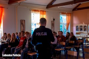 Zdjęcie przedstawia policjanta rozmawiającego z młodzieżą.