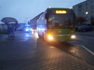 Na zdjęciu widoczny autobus, który zjeżdza do przystanku autobusowego. W tle widoczny radiowóz z włączonymi sygnałami świetlnymi.