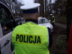 Zdjęcie przedstawia dwóch policjantów kontrolujących kierowcę. W tle stoi bus Inspekcji Transportu Drogowego