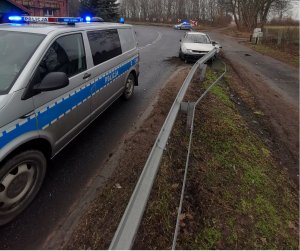 radiowóz z włączonymi sygnałami świetlnymi, za nim biały pojazd po zdarzeniu