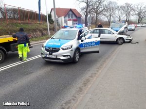 radiowóz z włączonymi sygnałami świetlnymi, laweta i biały pojazd