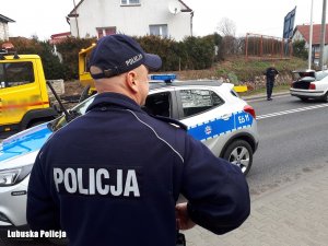 policjant stojący tyłem przy radiowozie,  z tyłu laweta