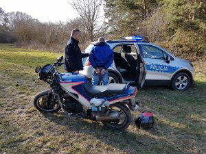 motocykl, w tle policjant prowadzący zatrzymanego do radiowozu