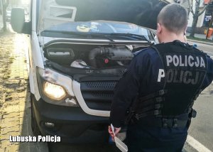 policjant stojący przed otwartą maską busa