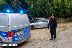 Radiowóz na sygnałach w tle policjant oraz auto uciekajacego