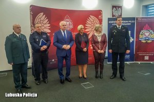 sześć osób stojących w pomieszczeniu, w tym umundurowany policjant