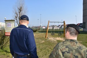 policjant stojący tyłem spoglądający na plac, obok stoi żołnierz