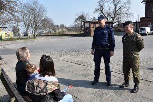 policjant i żołnierz rozmawiający z osobami siedzącymi na ławce