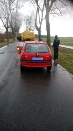 tył czerwonego samochodu stojącego na drodze, obok stoi policjant