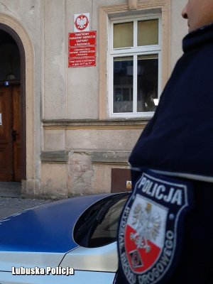 umundurowany policjant stojący przed budynkiem SANEPID-u