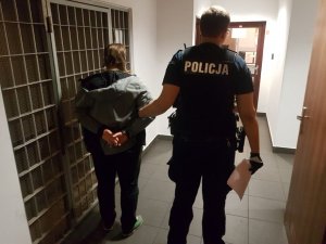 Policjant w mundurze trzymające za rękę zatrzymanego przy celi - widok z tyłu