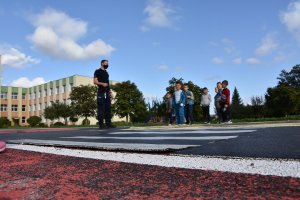 Policjanci na placu do nauki jazdy rowerem uczą pierwszoklasistów przechodzenia przez drogę.