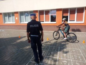 Policjanci na placu do nauki jazdy rowerem uczą pierwszoklasistów przechodzenia przez drogę.