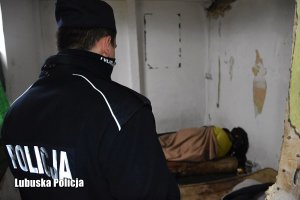 Policjant w opuszczonym budynku widzi śpiącego na materacu bezdomnego, przykrytego kocem.