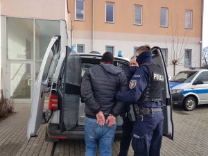 dwójka policjantów wprowadza do przedziału dla zatrzymanych mężczyznę, który na rękach ma założone kajdanki.