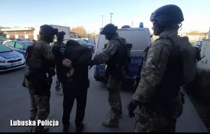 Policjanci prowadzą zatrzymanego do radiowozu z komendy