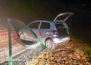 Auto osobowe najechało i przewróciło przęsło płotu metalowego, w tle w nocy pola