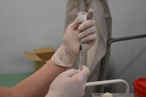 Dłonie w rękawiczce, pielęgniarka trzyma fiolkę jednoczesnie strzykawką nabiera dawkę