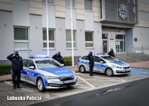 Dwa radiowozy na sygnałach wraz z e stojącymi po ich obu bokach policjantami na baczność oddającymi honory, w tle budynek komendy wojewódzkiej