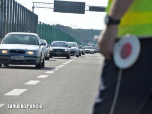 Część sylwetki policjanta stojącego na drodze, z tarczą do zatrzymywania pojazdów