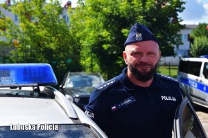 Policjant stojący przy radiowozie na parkingu w furażerce