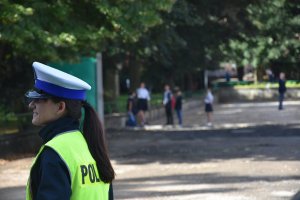 Policjantka ruchu drogowego na tle placu przed szkoła na którym biegają dzieci