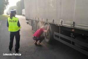 Policjantka patrząca na kierowcę ciężarówki, który sprawdza uszkodzone koło ciężarówki