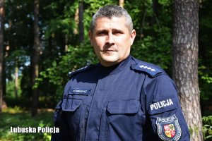 Policjant w mundurze widziany od pasa w górę, w tle las