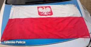Leżąca na radiowozie flaga polski, widoczne są na niej przerwania i uszkodzenia.