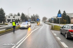 Ulica, widok na przejście dla pieszych, za przejściem stoi pojazd osobowy oraz radiowóz, troje policjantów wykonuje czynności