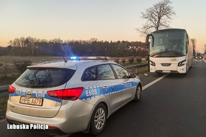 Przy poboczu drogi stoi autokar i radiowóz na sygnałach.