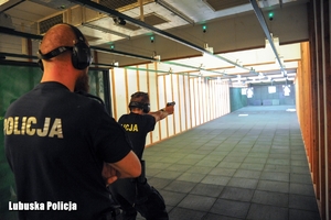 Policjanci na strzelnicy, jeden celuje do tarczy a instruktor go nadzoruje.