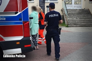 kobieta w asyście policji i ratownika medycznego wsiada do karetki