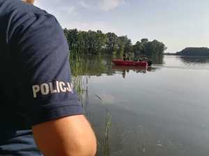 łódka na jeziorze na tle policjanta