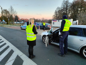 Policjanci wraz z pracownikami w kamizelkach z Gminy prowadzą działania na drodze przy pojazdach