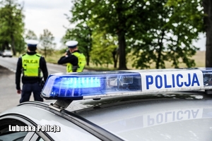 Dach radiowozu i w tle policjanci.