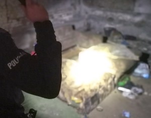 Policjant świecący latarką na miejsce gdzie mogła nocować osoba bezdomna.