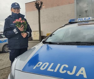 Policjantka z kwiatami przy radiowozie.