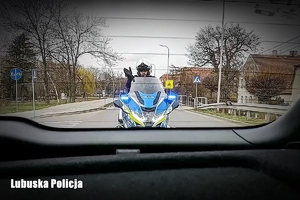 Policjant na oznakowanym motocyklu widziany przez tylną szybę auta