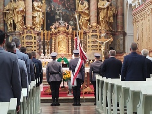 Widok na ławki z policjantami oraz gośćmi podczas mszy, widać ołtarz, kapelana i wychodzący poczet sztandarowy