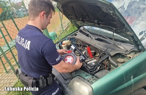 Policjant przy zielonym aucie, pomaga je uruchomić