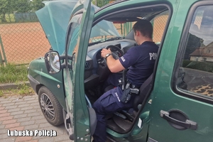 Policjant przy zielonym aucie, pomaga je uruchomić